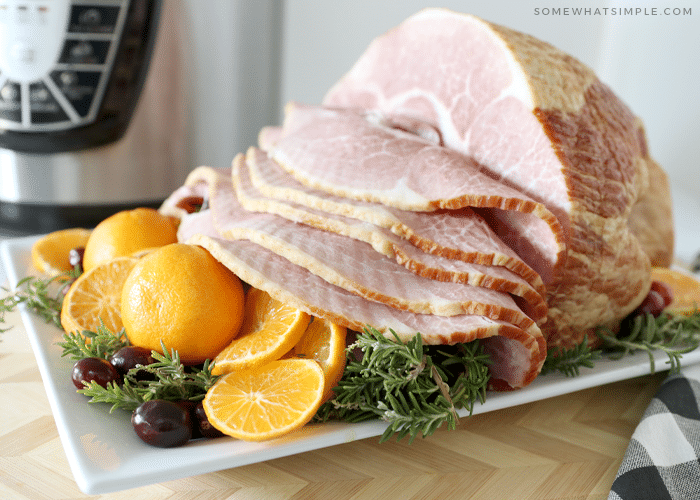 an Instant Pot Ham on a white tray with a basket of rolls 