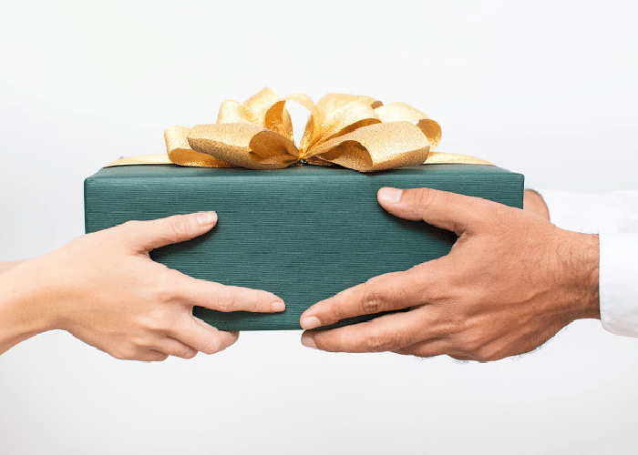 woman handing man a valentine gift box wrapped in green paper and a gold bow