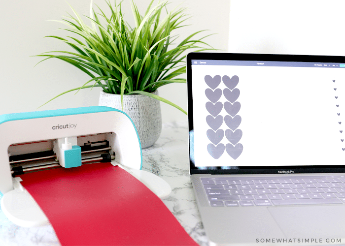 laptop with hearts on the screen next to a Cricut Joy machine with red vinyl