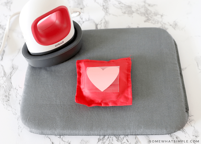 red bean bag with pink heart in the center on a gray mat with mini iron