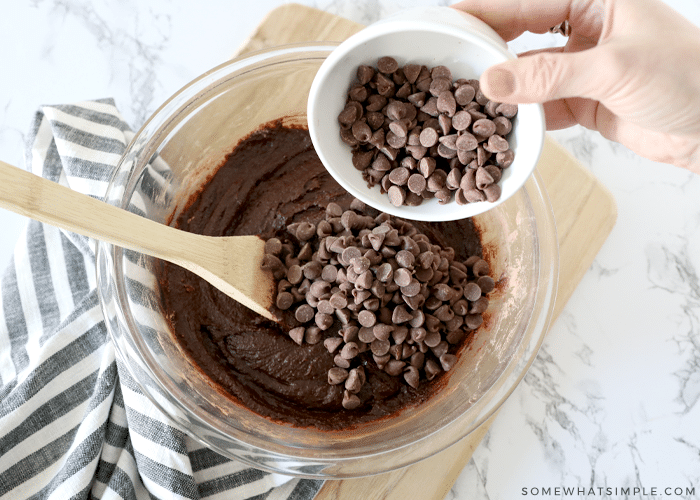 cup of chocolate chips being held over a bowl of brownie batter