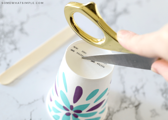 scissors poking a hole in the bottom of a paper cup