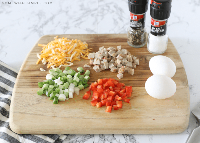 eggs, cheese, sausage, green onions, red bell peppers, salt and pepper on a cutting board