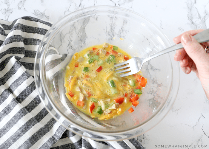 glass bowl with eggs and omelet toppings being mixed with a fork