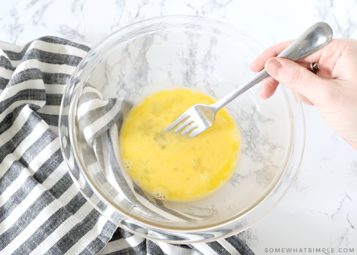 glass bowl with egg being mixed with a fork