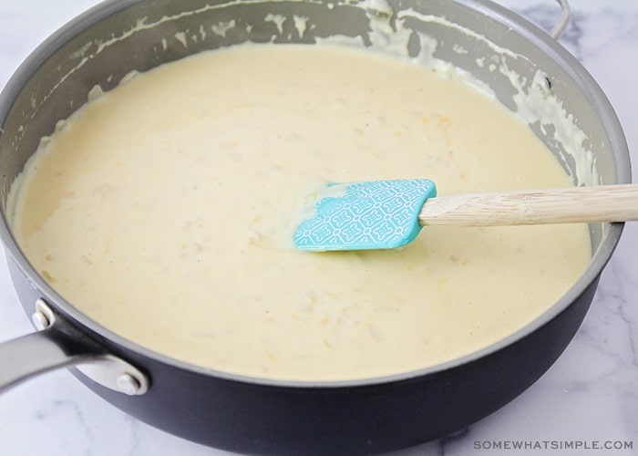 a sauce pan with a spatula stirring a creamy white sauce.