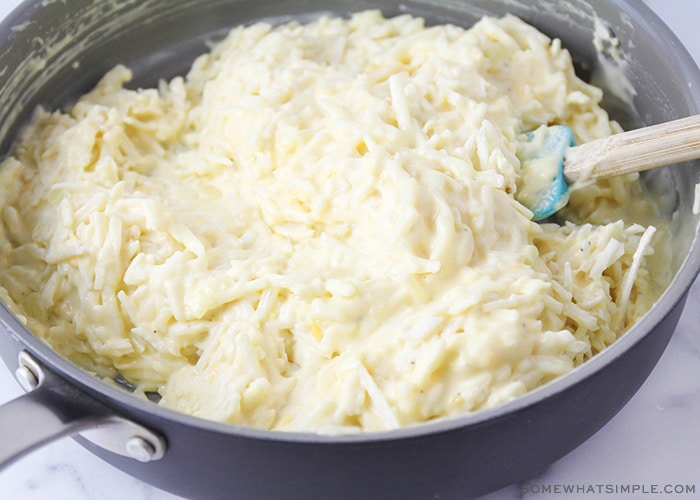 frozen hash brown potatoes in a sauce pan mixed with a white sauce