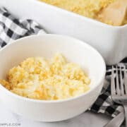 white bowl with a serving of cheesy potato casserole with casserole pan in background