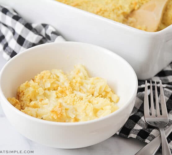 white bowl with a serving of cheesy potato casserole with casserole pan in background