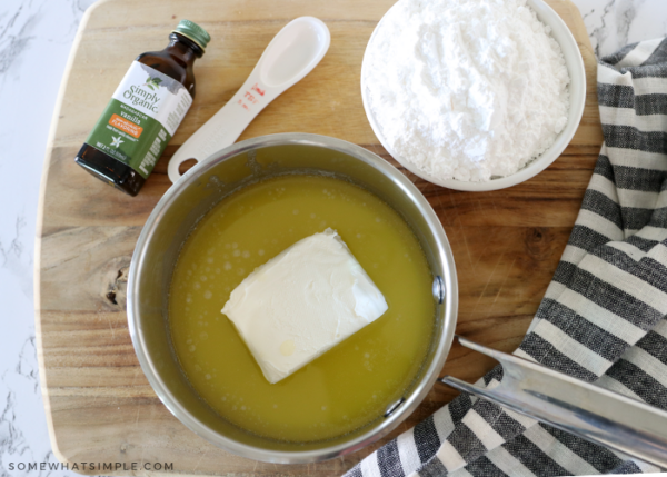 melted butter in a pot with cream cheese inside. the pot is laying next to vanilla and powdered sugar