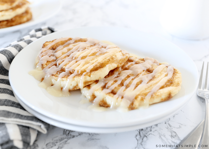 two cinnamon roll pancakes on a white plate and striped napkin