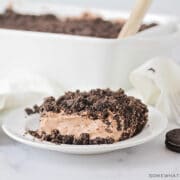 slice of chocolate cake with crushed oreos on top and the full cake in the background