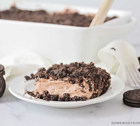 slice of chocolate cake with crushed oreos on top and the full cake in the background
