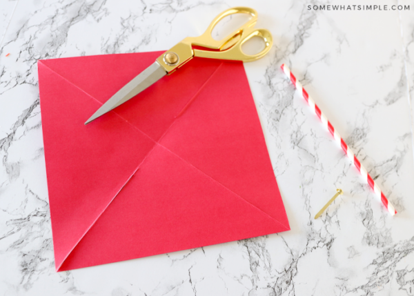 red piece of paper with gold scissors and a paper straw