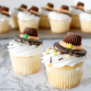 2 pilgrim hat cupcakes on the counter with a tray of more cupcakes in the background