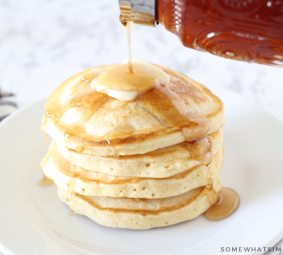 pouring syrup on top of a stack of pancakes with a slab of butter