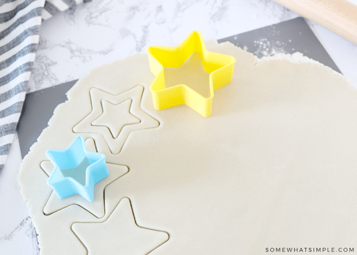 smaller blue cookie cutter next to a larger yellow cutter on top of sugar cookie dough