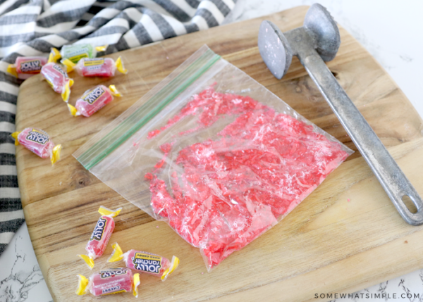 bag of crushed jolly rancher candies on a cutting board next to a metal mallet