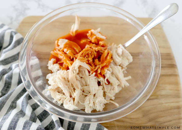 mixing chicken with buffalo sauce in a glass bowl