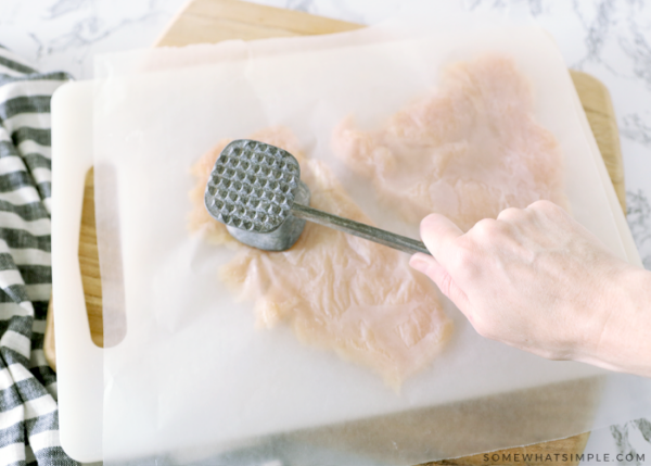 pounding raw chicken with a metal meat tenderizer