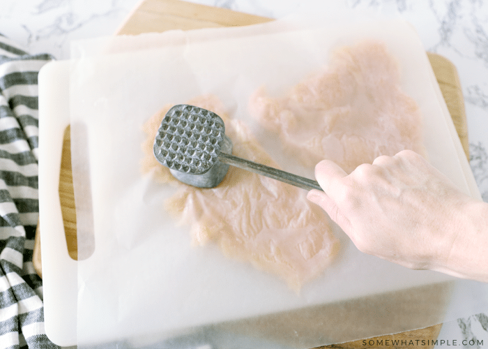 pounding raw chicken with a metal meat tenderizer 