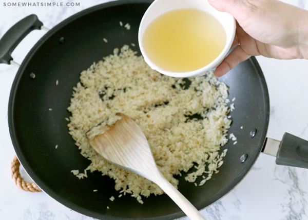 adding chicken broth to a pot of rice