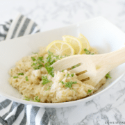 white bowl next to striped napkin with a wooden spoon inside parmesan risotto