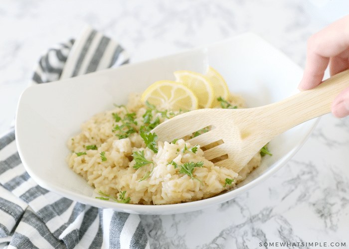 white bowl next to striped napkin with a wooden spoon inside parmesan risotto