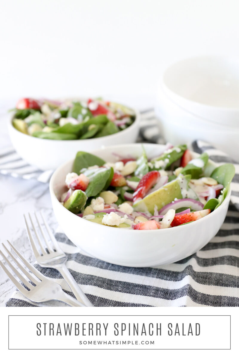 2 white bowls filled with strwberry spinach salad with avocado and red onion