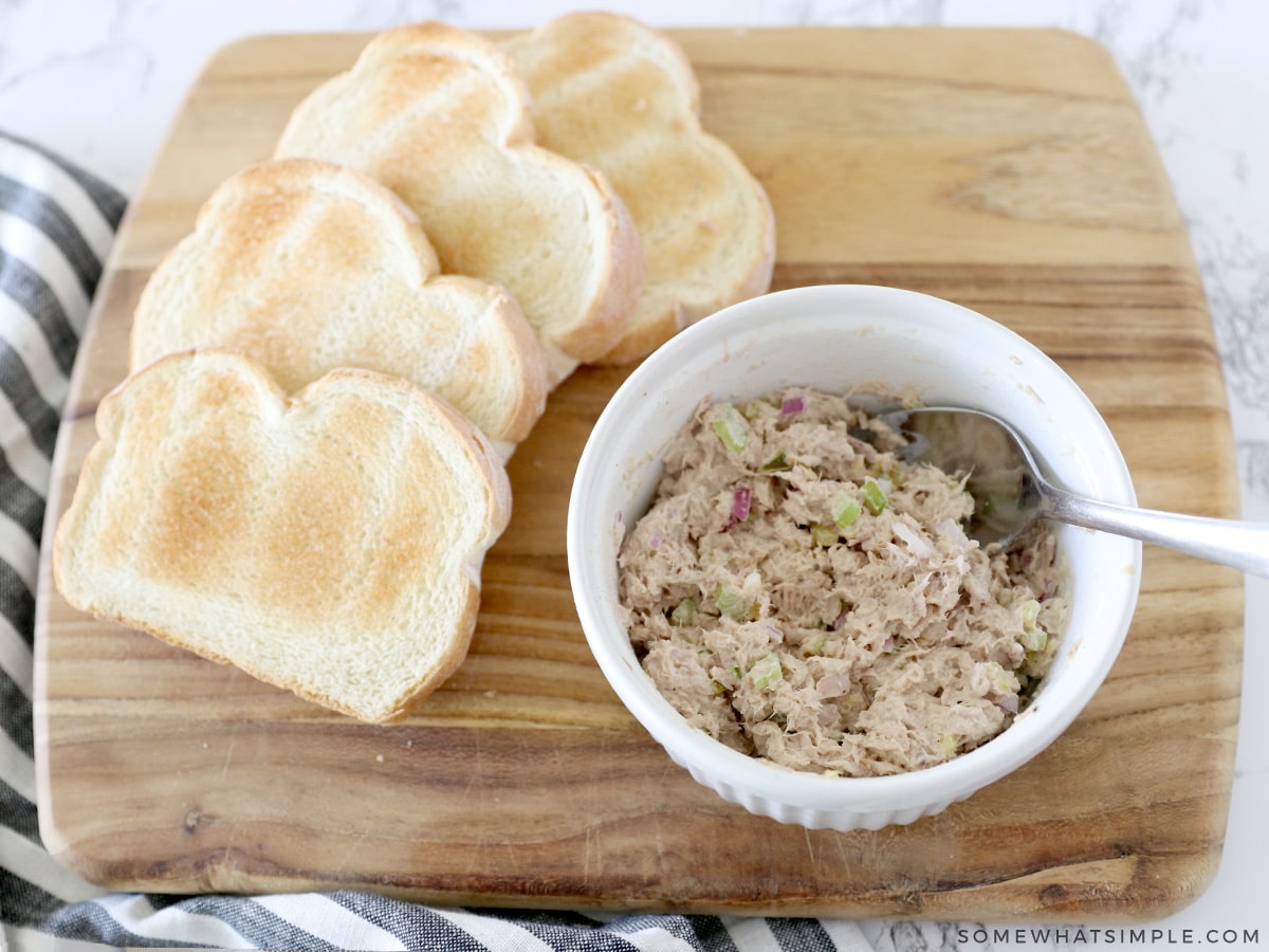 mixing tuna salad in a white bowl next to toast