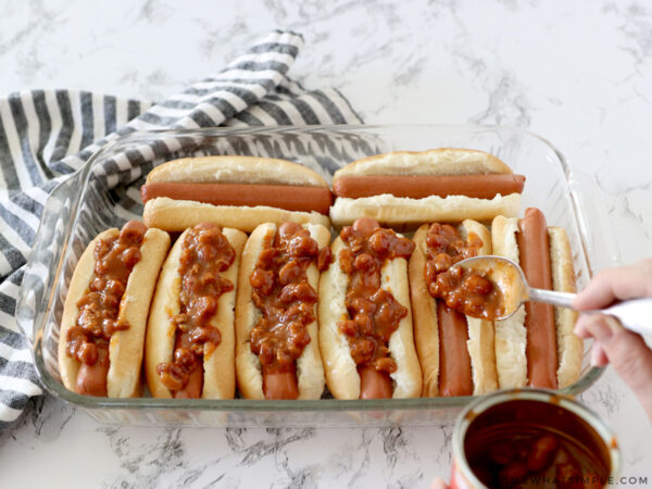 chili dogs in a baking dish gettting covered with chili