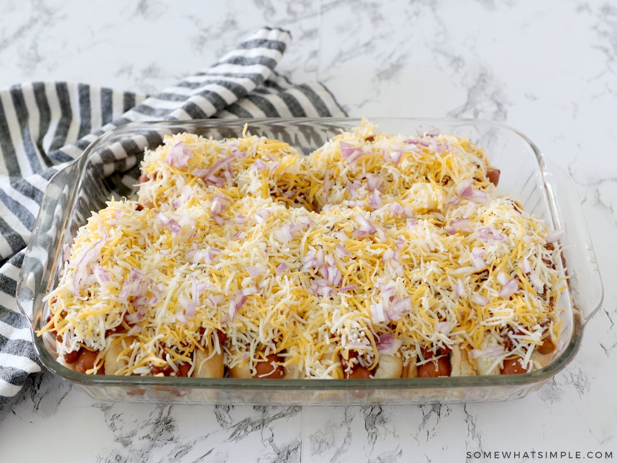 adding cheese to a baking pan of chili dogs