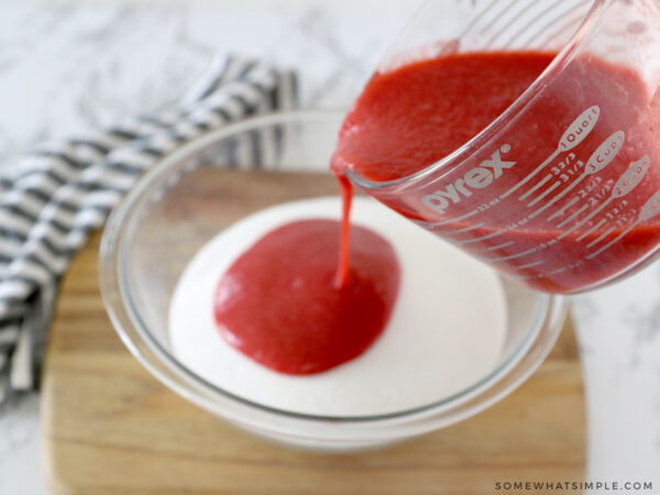 adding pureed strawberries to a bowl of sugar