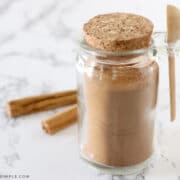 apple pie spice in a jar with cinnamon sticks behind it