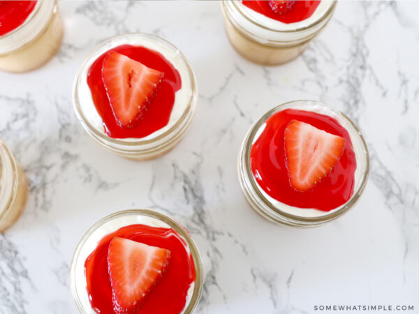 adding strawberry glaze and a sliced strawberry to a cake in a jar