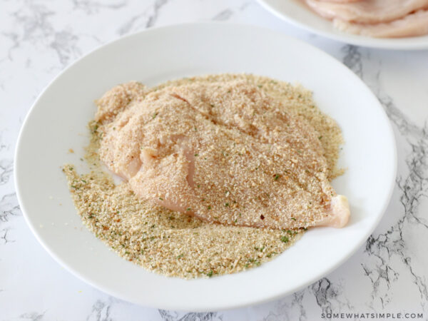 pressing raw chicken into bread crumb mixture