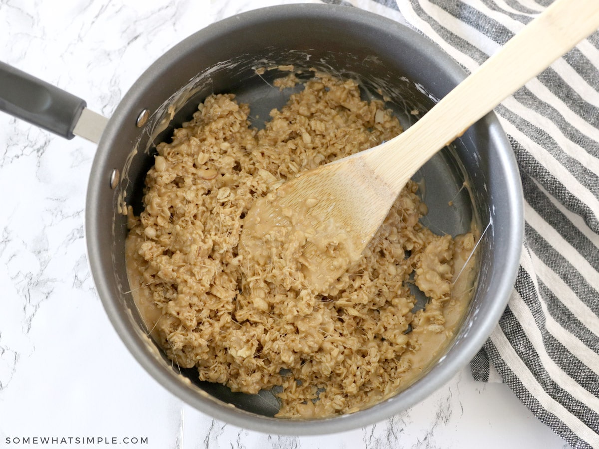 adding granola to peanut butter and marshmallow mixture in a sauce pan