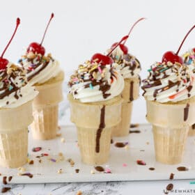 ice cream cone cupcakes in a row with chocolate syrup and a cherry