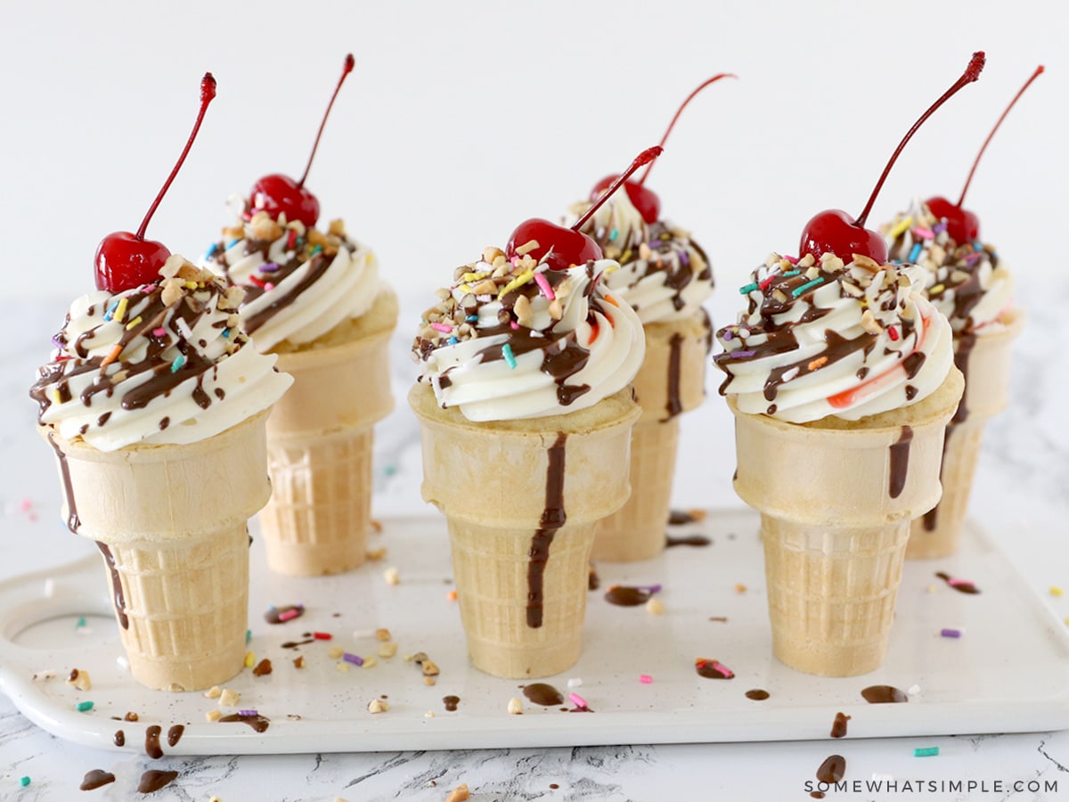 ice cream cone cupcakes in a row with chocolate syrup and a cherry