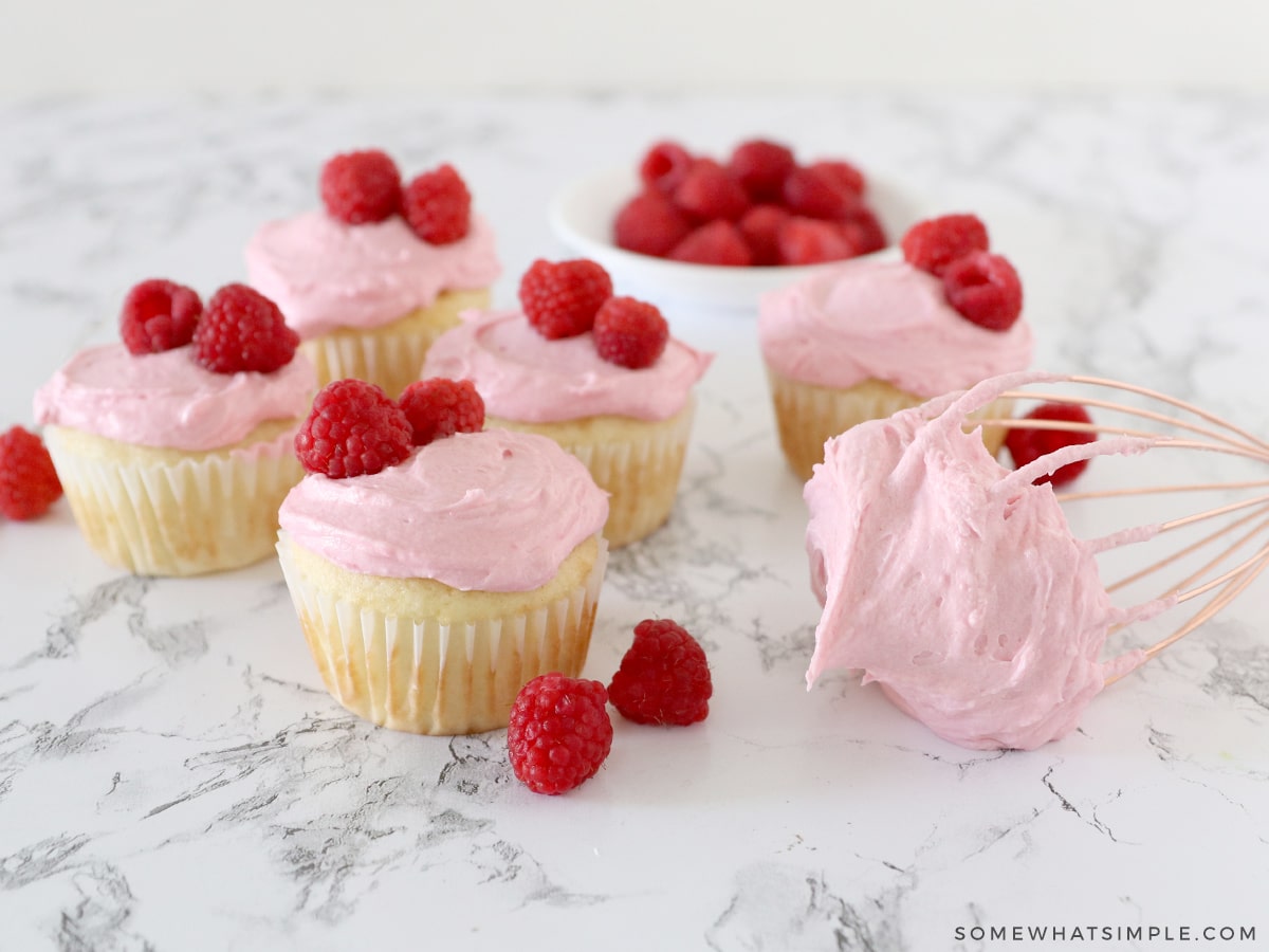 6 vanilla cupcakes on the counter with raspberry frosting on top