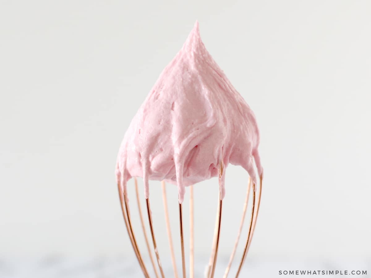 raspberry buttercream frosting on top of a gold whisk