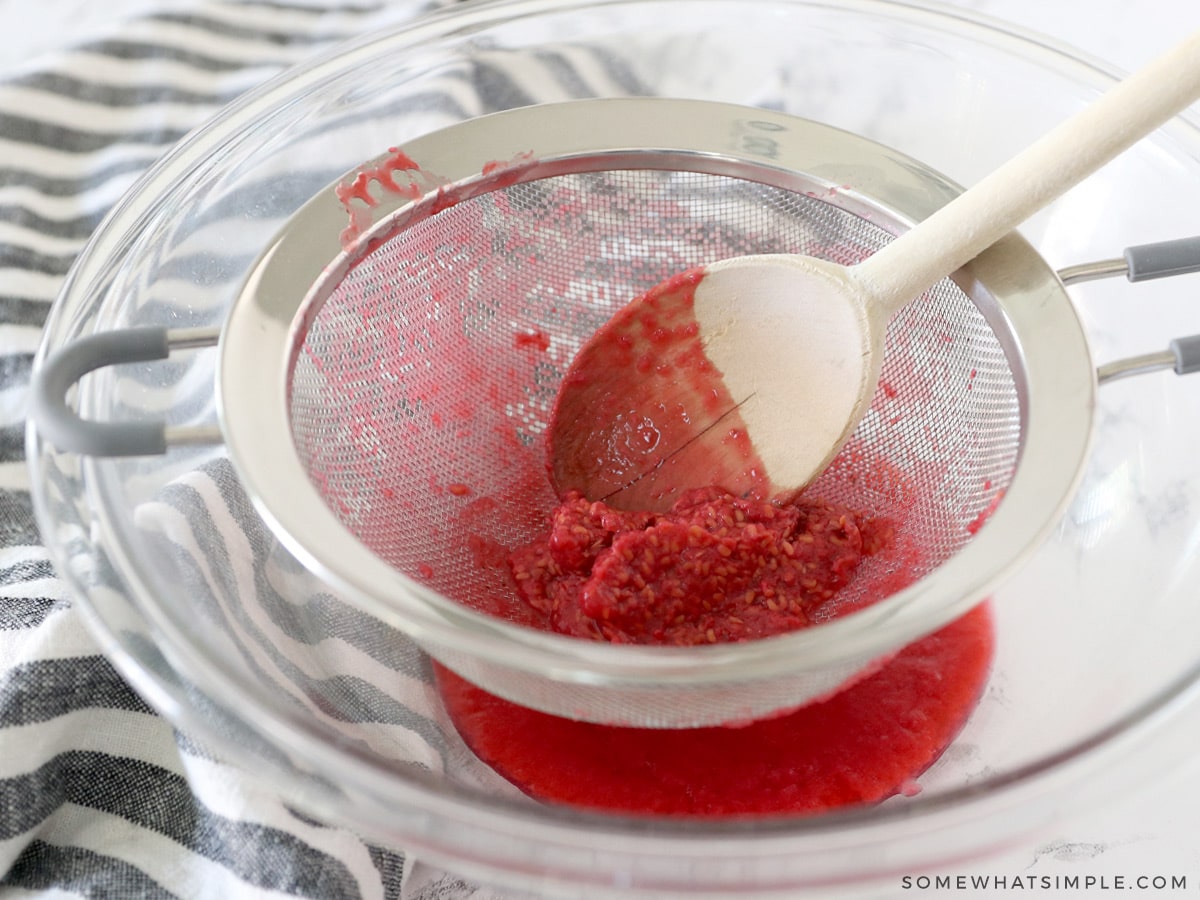 separating the raspberry seeds from the juice with a strainer and a wooden spoon over a glass bowl