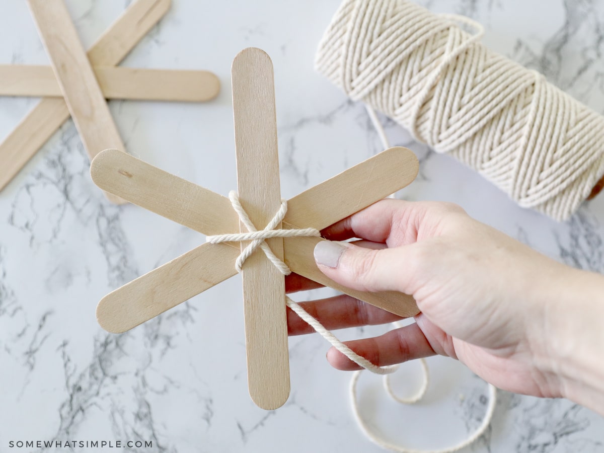 adding yarn to popsicle sticks to make a spider web