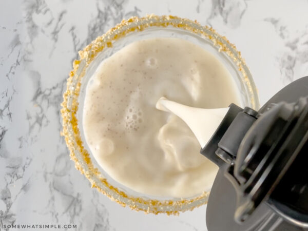 pouring a milk mocktail into a cocktail glass lined with graham crackers