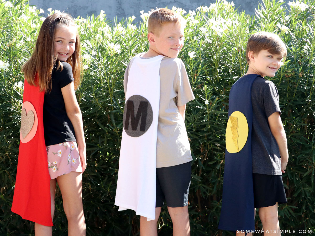 3 kids wearing superhero capes outside