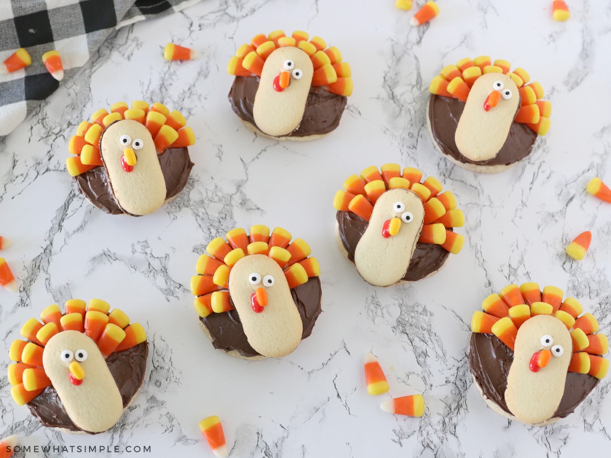 several turkey cookies laying on a white counter with candy corn sprinkled about