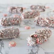 several marshmallow pops covered in chocolate laying on a counter with peppermint candies around them