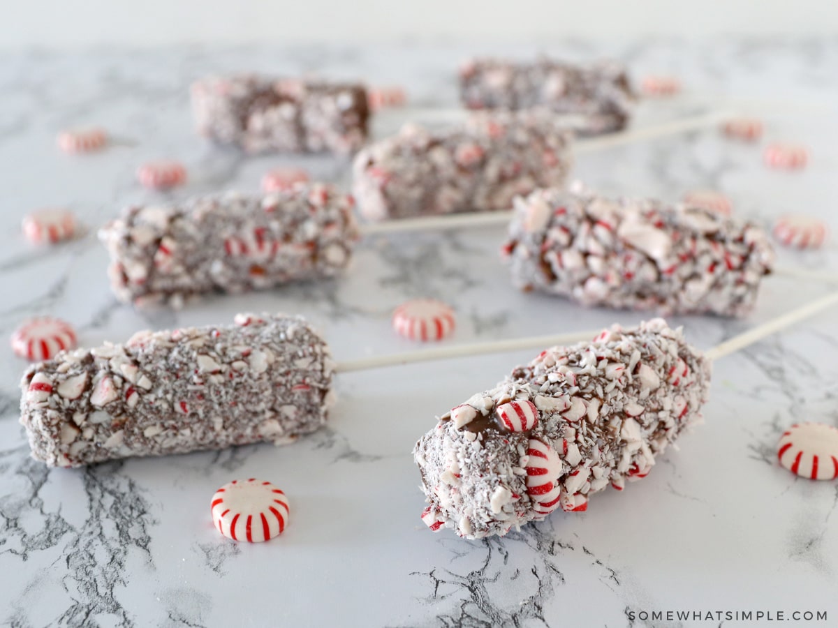 several marshmallow pops covered in chocolate laying on a counter with peppermint candies around them