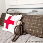 close up of a stuffed monkey on a bed with gray bedding and a swiss cross pillow