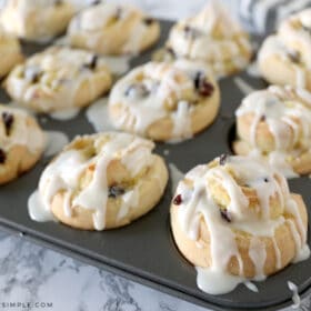 cranberry orange sweet rolls in a muffin tin drizzled with glaze